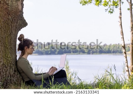Work from anywhere. Remote freelancer work in nature. Young woman, female freelancer working with laptop with Beautiful view of forest and lake. freelancer paradise, freedom of teleworking. distance Royalty-Free Stock Photo #2163133341