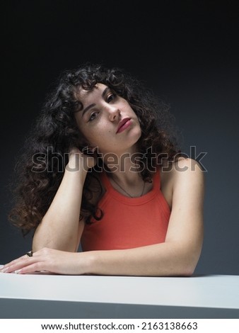 Portrait pictures of young beautiful woman with curly hair behind desk. A single light setup was used for portraits taken with the expression of emotions.