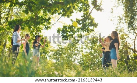 Cheerful schoolgirls play ball on a summer evening outside the city.
