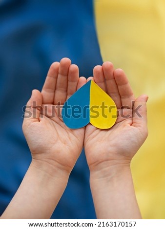 
A heart-shaped badge depicting the State Flag of Ukraine as a symbol of patriotism and pride in one's country. State symbol of Ukraine in children's hands against the background of the Ukrainian flag