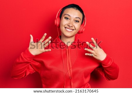 Beautiful hispanic woman with short hair listening to music using headphones showing and pointing up with fingers number nine while smiling confident and happy. 