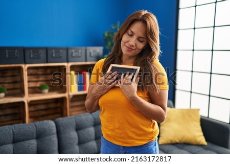 Young latin woman smiling confident hugging photo at home