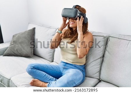 Young latin woman playing video game using virtual reality glasses at home