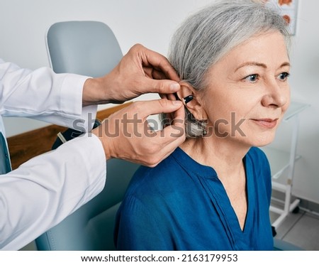 Senior woman during installation hearing aid into her ear by her audiologist, close-up. Hearing treatment for hearing impaired people Royalty-Free Stock Photo #2163179953