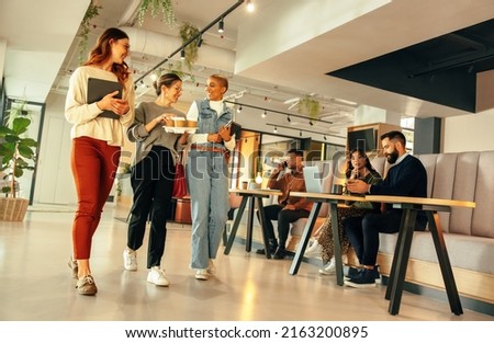 Smiling businesswomen walking through a modern office in the morning. Group of young businesswomen having a cheerful chat. Happy female entrepreneurs working together in a co-working space. Royalty-Free Stock Photo #2163200895