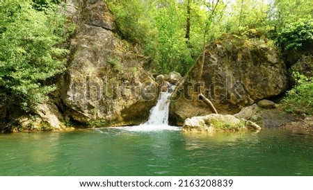 Forest landscape with a small lake in summer season. Selective focus, waterfall is out of focus.