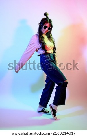The cute young Asian girl with casual clothes posing under the gel color lightning in studio.