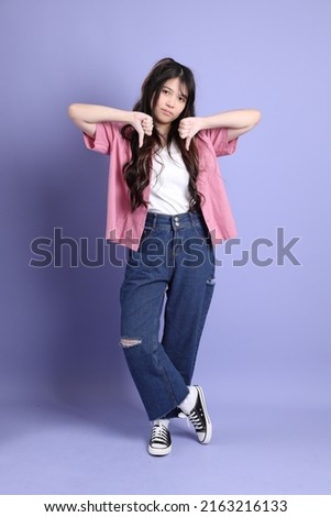 The cute young Asian girl with casual clothes standing on the purple background.