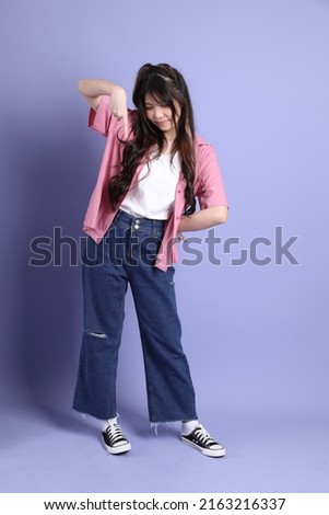 The cute young Asian girl with casual clothes standing on the purple background.