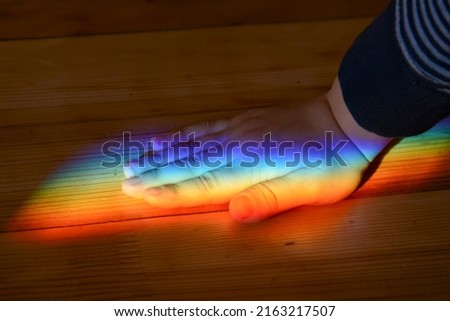 Kids hand under rainbow color sun beam on wooden plank texture. Physical light split effect studying.