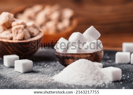 Bowl and scoop with white sand and lump white sugar on wooden background. Sugar cube. Make unhealthy nutrition, obesity, diabetes, dental care and much more.