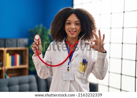 Young african american doctor woman wearing doctor uniform and stethoscope doing ok sign with fingers, smiling friendly gesturing excellent symbol 