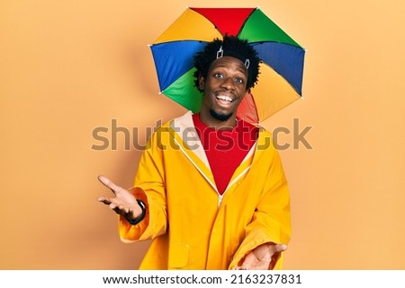 Young african american man wearing yellow raincoat smiling cheerful offering hands giving assistance and acceptance. 