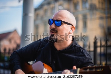 Interesting bearder man wearing sunglasses playing guitar on the street. retro style. Lifestyle, real people concept.