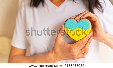 Close-up of Woman hold heart shape gingerbread cookie with ukrainian flag colors in hands