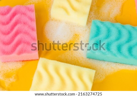top view of textured multicolored sponges and foam on bright yellow background.