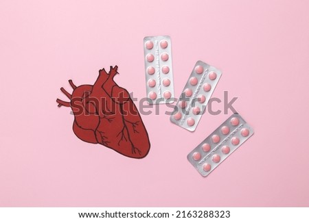 Treatment of cardiovascular disease concept. Paper cut anatomical heart with stethoscope and pills on pink background. Top view
