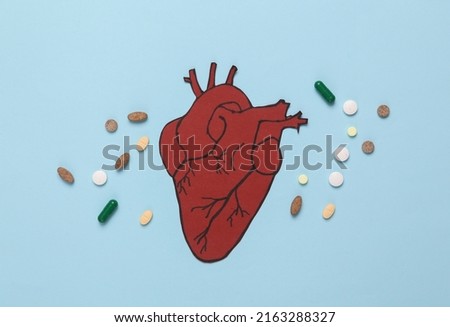 Treatment of cardiovascular disease concept. Paper cut anatomical heart with stethoscope and pills on a blue background. Top view