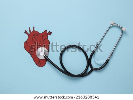Diagnosis and treatment of cardiovascular disease. Stethoscope examining of paper heart health. Blue background. Top view. Flat lay