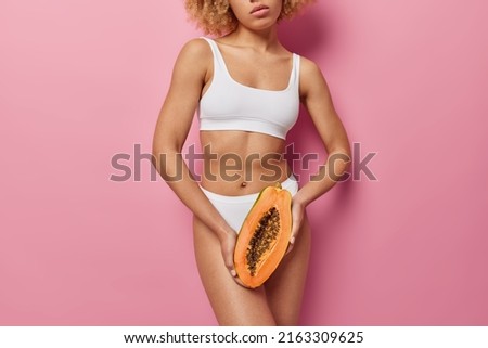 Healthy skin and moisturising concept. Unknown faceless woman holds half of papaya fruit wears white cropped top and panties going to make natural facial mask poses indoor. Antioxidant cosmetic