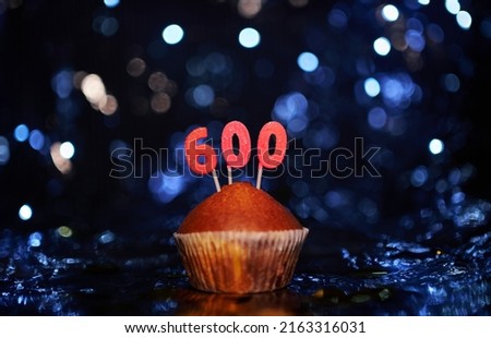 Digital gift card birthday concept. Tasty homemade vanilla anniversary cupcake with number 600 six hundred on aluminium reflecting foil and blurred background in minimalistic style. High quality image