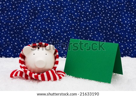 Piggy bank wearing a scarf on snow with blank card and a star background, Christmas savings