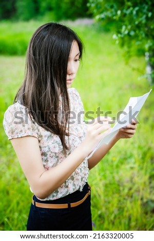 A lovely young woman of asian outerness writes a pen in a piece of paper on a background of summer green nature.