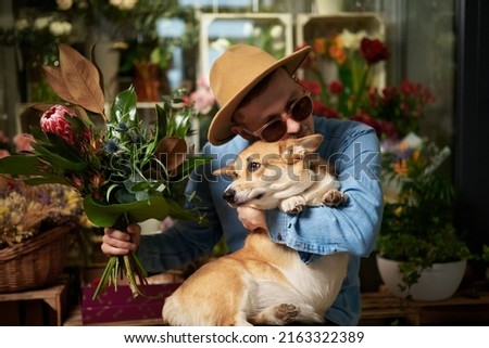Smiling hipster male person in sunglasses and hat with fresh spring flower bouquet and welsh corgi dog. Mother's Day, Valentine's Day or International Women's Day concept. High quality image
