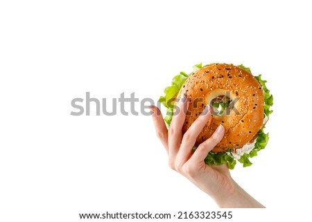 Bagel with prosciutto, cream cheese in woman hand. Holding a Sandwich with lettuce for breakfast on white background. Space for text Royalty-Free Stock Photo #2163323545