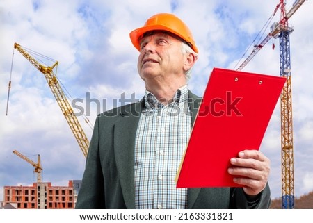 Construction supervisor, worker at a construction site. Manager wearing protective workwear, hard hat, construction cranes on skyline. Construction workforce, working labor man.