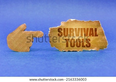 Business concept. On a blue surface, a cardboard hand points to a sign with the inscription - Survival Tools