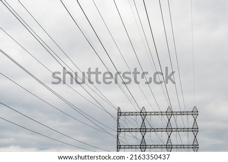 An electric utility pole with electrical wires, transmission lines, conductors, and distribution wires for high voltage electricity. The tall transmission lines have grey clouds in the background.