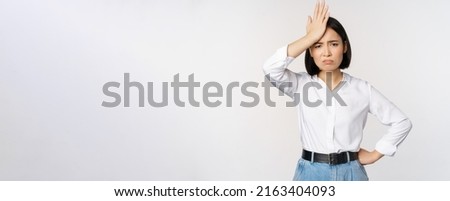Bothered and tired asian woman, looking complicated, slap forehead, facepalm sign and grimacing upset, looking distressed at camera, white background Royalty-Free Stock Photo #2163404093