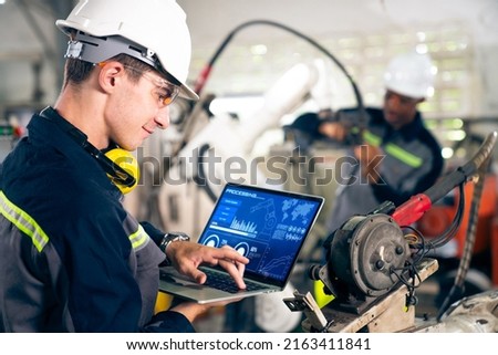 Young factory worker working with adept robotic arm in a workshop . Industry robot programming software for automated manufacturing technology . Royalty-Free Stock Photo #2163411841