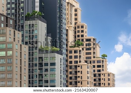 One lonely tree was planted on top of a high buildin in business center surrounded by tall skyscrapers with blue sky and white soft cloulds in background. Concept of nature living in city lifestyle. Royalty-Free Stock Photo #2163420007