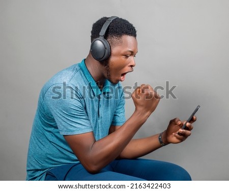 An African Man on Colored shirt with Headset while happy looking at his Mobile Device