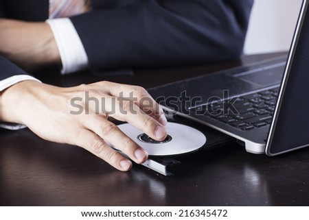 Business's hand holding Disk insert to laptop computer  Royalty-Free Stock Photo #216345472