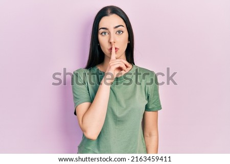 Beautiful woman with blue eyes wearing casual t shirt asking to be quiet with finger on lips. silence and secret concept. 