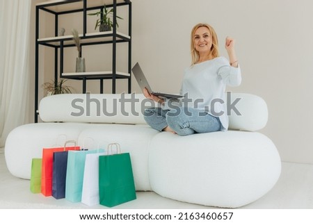 Portrait of mature attractive cute pretty cheerful woman sitting on sofa using laptop shopping. Woman happy shopping near her many shopping bags at home
