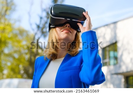Smiling woman in vr glasses experiencing augmented reality in front of a business center. Futuristic future in the metaverse world. 