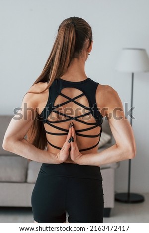 Rear view. Young woman with slim body type and in yoga clothes is at home.
