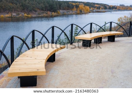 semicircular benches with wooden seats in autumn near a metal fence. autumn landscape in the park