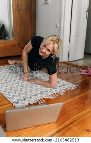 mature woman at home doing sport yoga on the floor with laptop online classes 