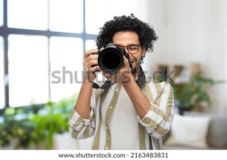 photography, profession and people and concept - happy smiling man or photographer in glasses with digital camera over home room background