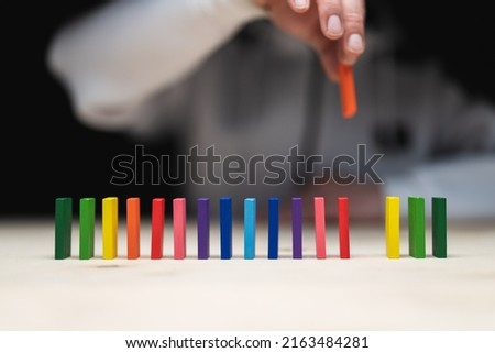 Conceptual photo of a hand placing a stone to a row of domino stones.
Domino effect with colored stones and copyspace