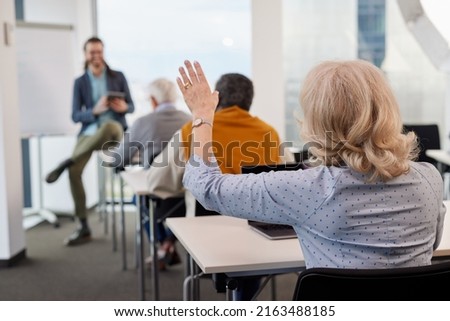 A senior woman is asking for an explanation in the computer course while sitting with elderly students in the classroom. Royalty-Free Stock Photo #2163488185