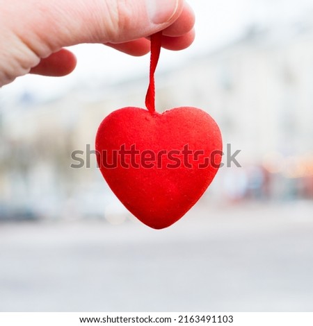 Red heart in hand close-up on the background of the city. Valentine's day preparation concept.