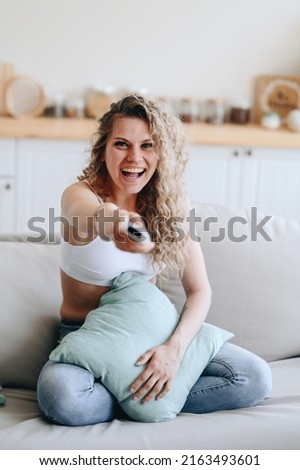 Vertical photo of a young woman sitting on a sofa holding bullets straight in her hands in a good happy mood. The concept of spending leisure time on the sofa