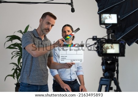Behind the Scenes on a Video Production Set. Director Uses Clapper Slate to Signify Action. Video Camera, Microphone and Lighting Can Be Seen During Interview