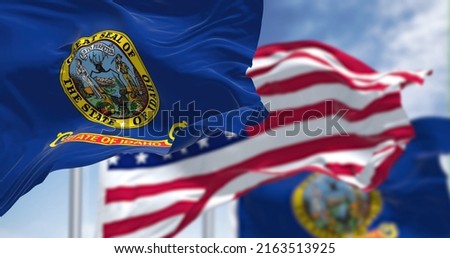 The Idaho state flag waving along with the national flag of the United States of America. In the background there is a clear sky. Idaho is a state in the Pacific Northwest region of the United States Royalty-Free Stock Photo #2163513925